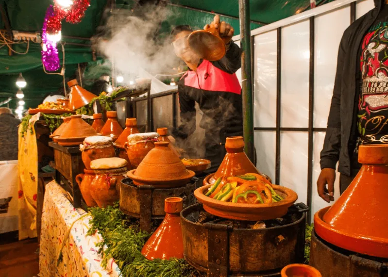 A man cooks on a table filled with various pots during a Morocco Food Tour, showcasing traditional culinary practices.