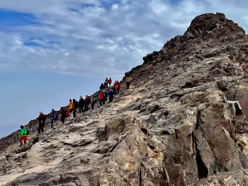 A group of hikers trekking up a mountain in the Atlas Mountains of Morocco, surrounded by rocky terrain and greenery.