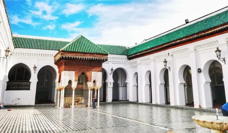 The beautiful courtyard of a Marrakech mosque, adorned with detailed mosaics and greenery, a key attraction in Fes, Morocco.