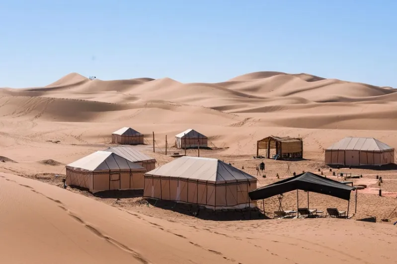 Luxury tents set against sand dunes and mountains in a Moroccan desert landscape.