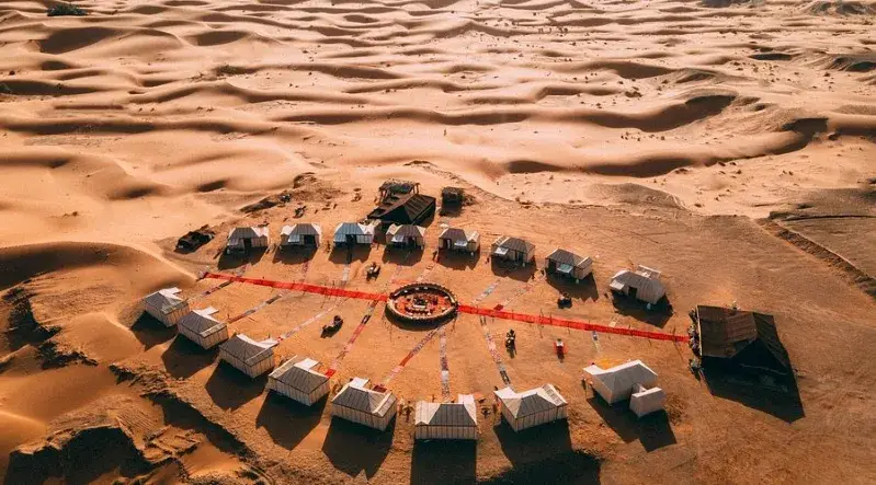 Aerial view of a luxury desert camp featuring several elegant tents set against a vast sandy landscape.