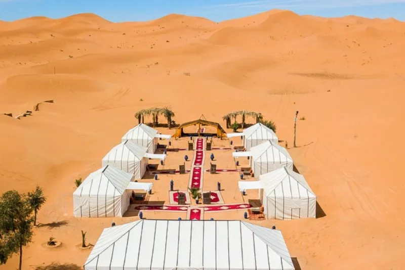 Aerial view of a wedding ceremony set in the Sahara Desert, showcasing the vast landscape and elegant decorations.