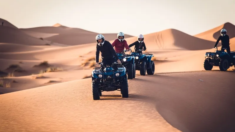 Four people riding quad bikes across a sandy desert landscape during a Marrakech tour.
