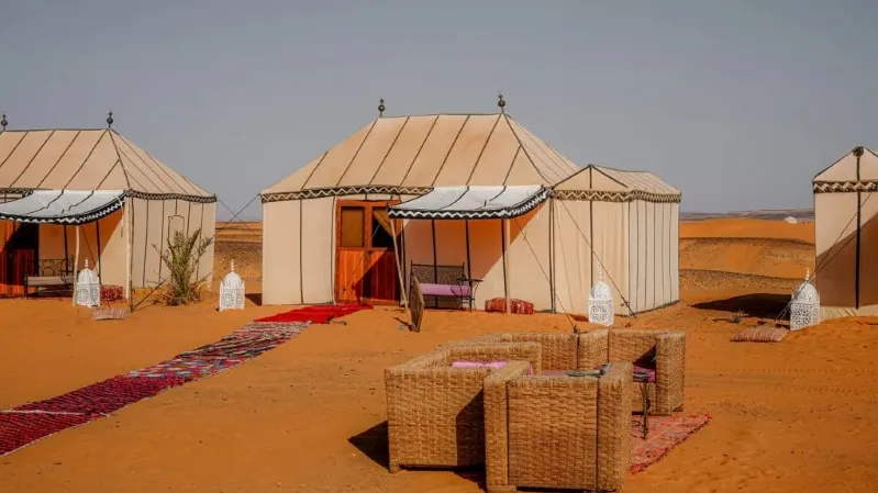 A luxury camp in the Moroccan desert featuring tents and a decorative rug on the sandy ground.