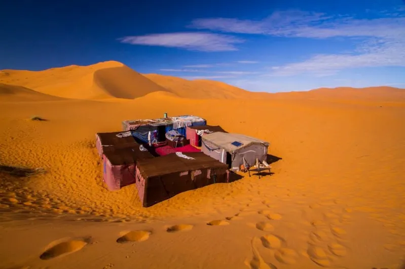 A tent in a desert luxury camp Morocco, surrounded by sand dunes under a clear blue sky.