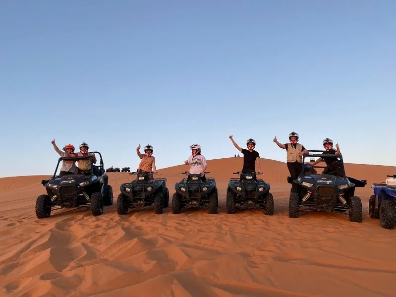 Four people on ATVs in the desert, joyfully raising their hands during a tour in Marrakech. 