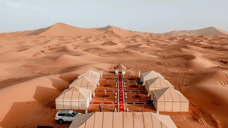 A desert camp featuring tents and a car, showcasing a scenic setup for desert tour marrakech.