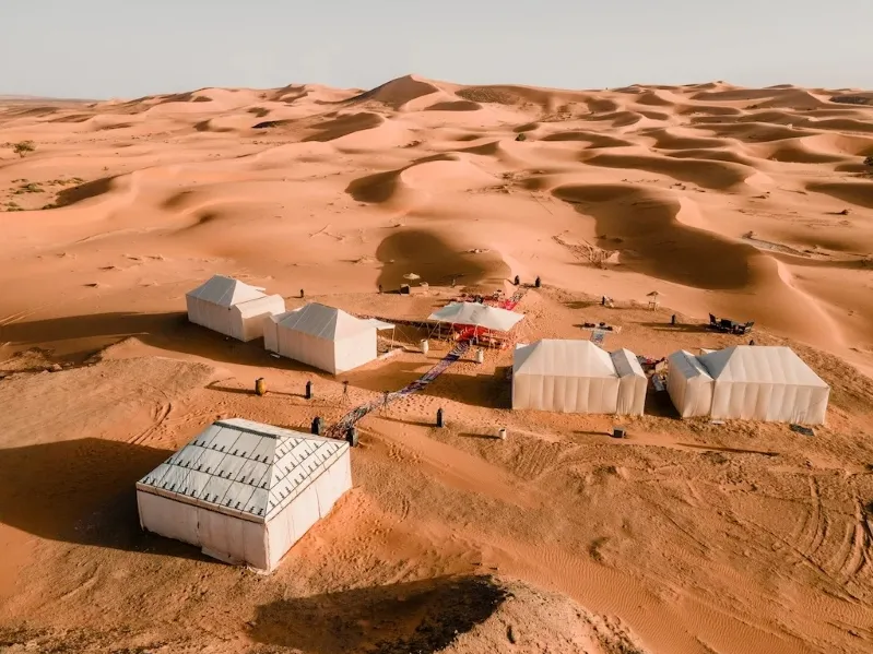A Morocco desert luxury camp featuring tents and a distinctive white roof under a clear blue sky.