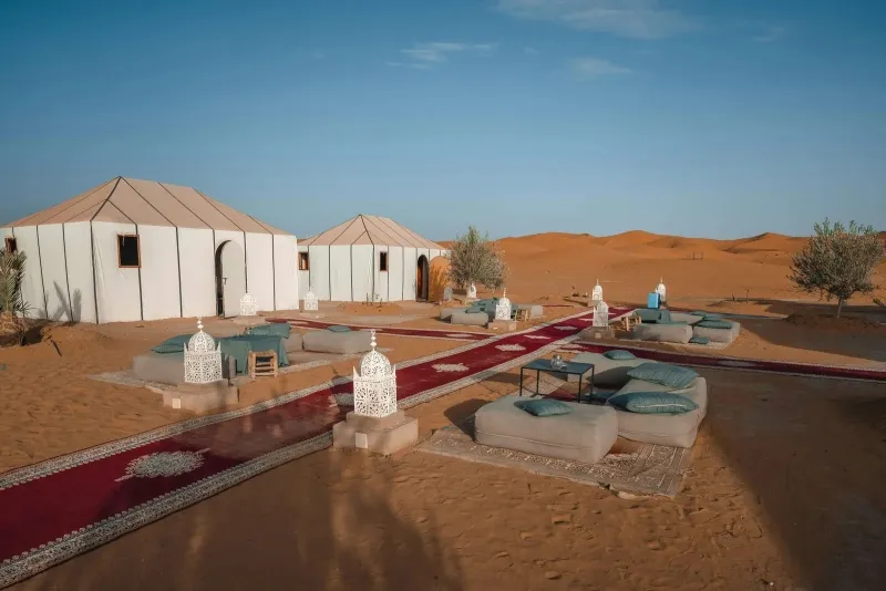 A desert camp featuring a red carpet and white tents, set against the backdrop of Morocco's Fes to Marrakech route.